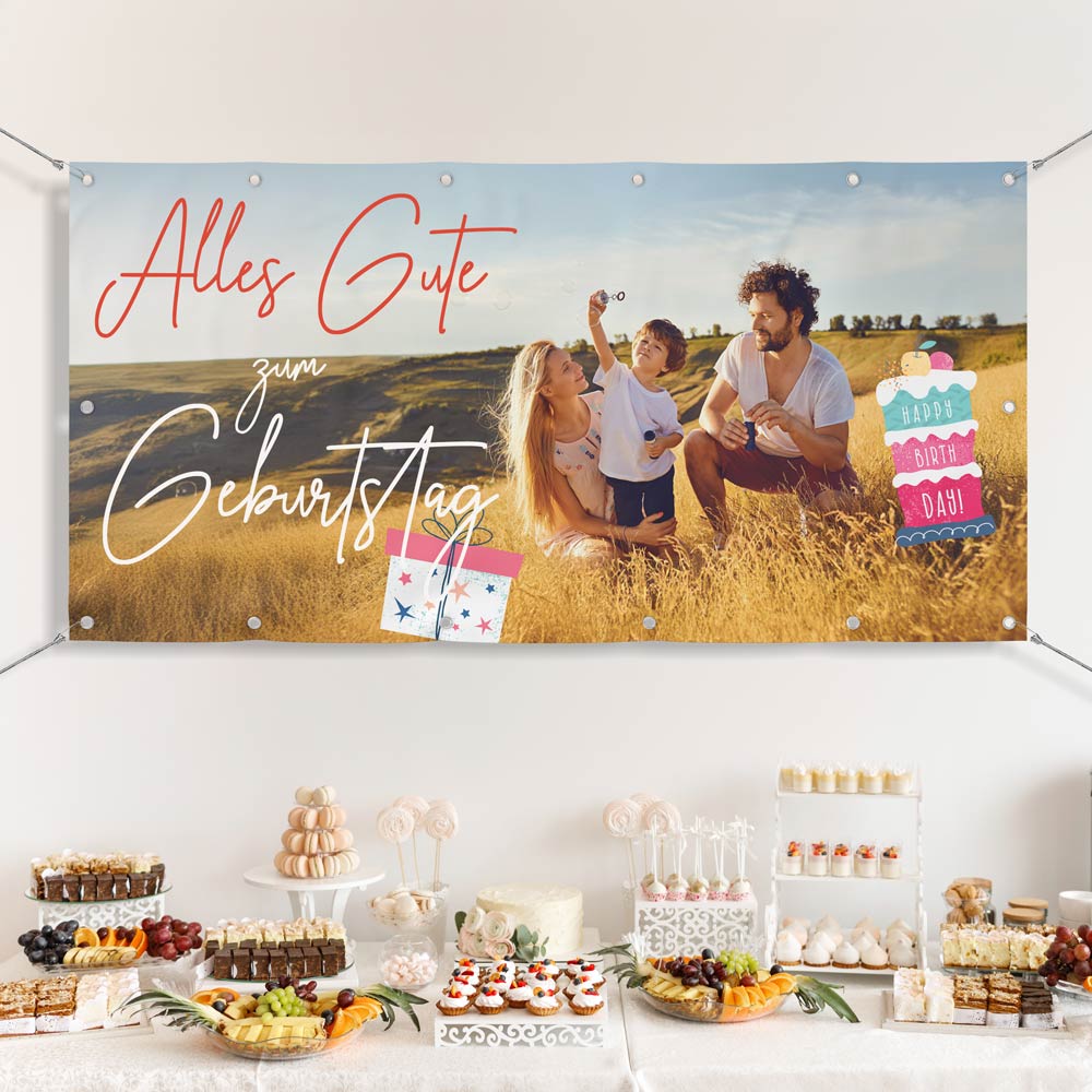 Großes personalisierbares Geburtstagsbanner mit dem Schriftzug 'Alles Gute zum Geburtstag', Geschenk- und Kuchengrafiken sowie einem Familienfoto auf einer Wiese. Das Banner ist über einem festlich dekorierten Buffet mit süßen Leckereien gespannt. Ideal als individuelle Geburtstagsdekoration für Feiern.