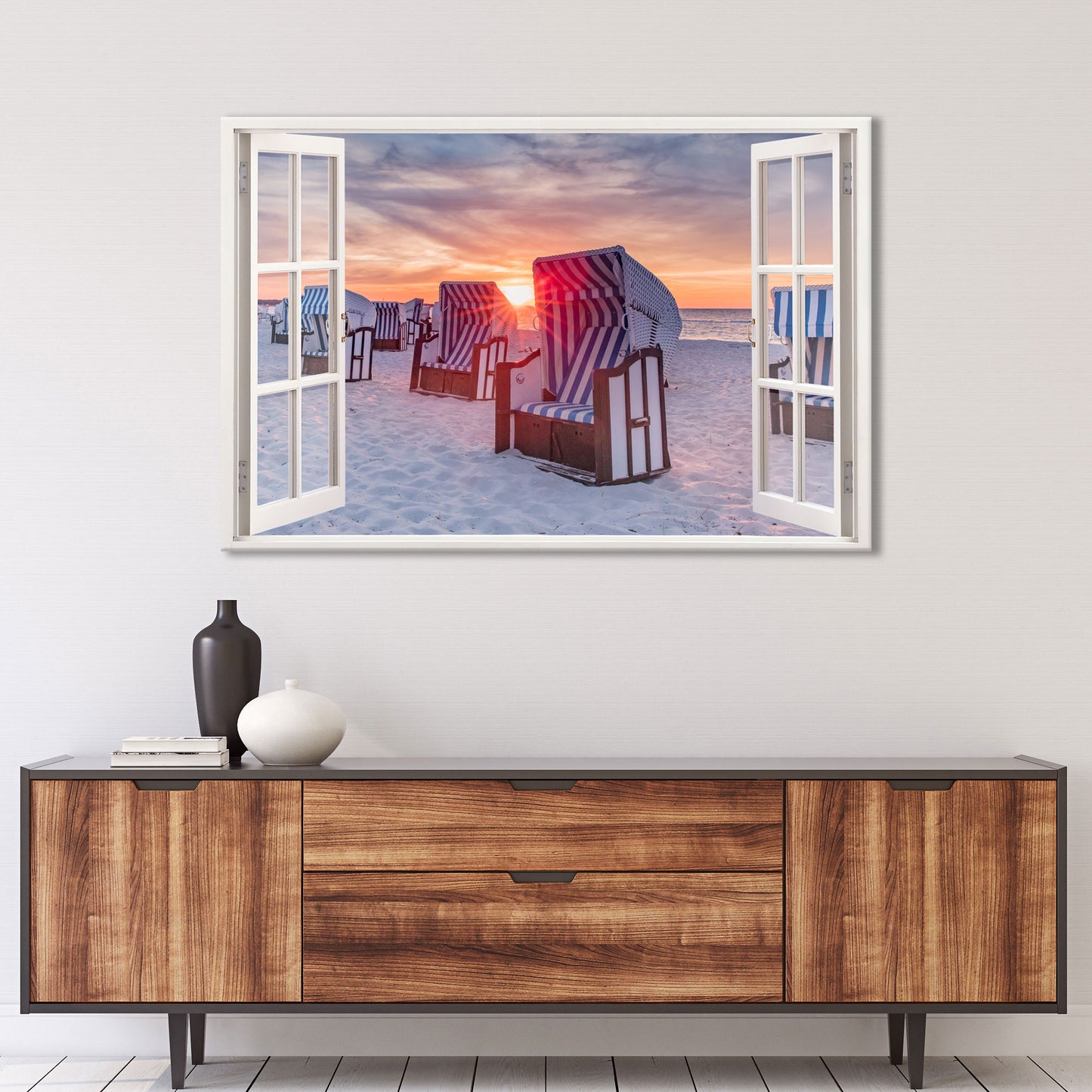 Wandbild mit Blick durch ein offenes Fenster auf einen Sandstrand mit Strandkörben im Sonnenuntergang. Die blau-weiß gestreiften Körbe stehen im warmen Licht der untergehenden Sonne, während das Meer den Himmel in sanften Orange- und Lilatönen spiegelt. Perfekte Wanddekoration für eine entspannte Atmosphäre.
