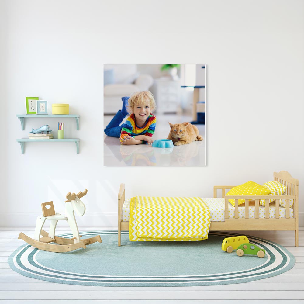 Modern eingerichtetes Kinderzimmer mit einem Bett, einem Schaukelpferd und Regalen. An der Wand hängt eine personalisierte Fotoleinwand mit einem fröhlichen Kind in buntem Pullover, das neben einer Katze liegt. Die Wanddekoration verleiht dem Raum eine individuelle und gemütliche Atmosphäre.