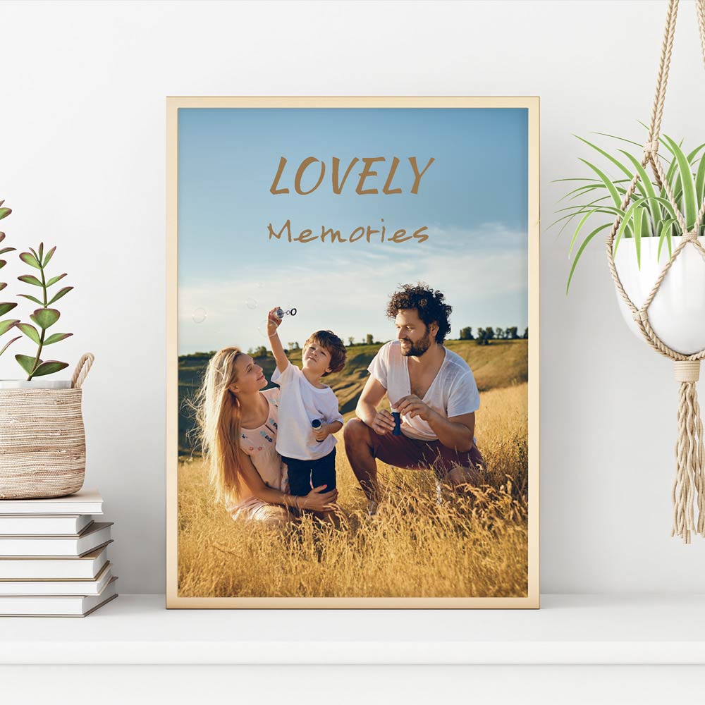 Gerahmtes personalisierbares Poster mit dem Schriftzug 'Lovely Memories' und einem Familienfoto auf einer Wiese. Das Bild steht auf einem weißen Regal, dekoriert mit gestapelten Büchern, einer Pflanze im Korb und einem hängenden Makramee-Blumentopf. Perfekt für stilvolle Wanddekoration und persönliche Erinnerungen.