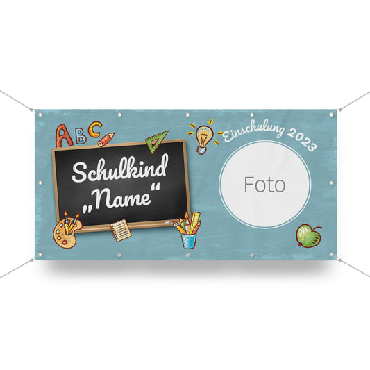 Personalisierbares Einschulungsbanner mit einer Kreidetafel, auf der "Schulkind 'Name'" geschrieben steht. Um die Tafel herum befinden sich Schulmotive wie Buchstaben, Bleistifte, ein Apfel und eine Glühbirne. Rechts ist ein runder Platzhalter mit der Aufschrift "Foto" für ein individuelles Bild. Darüber steht "Einschulung 2023". Das Banner hat einen blauen Hintergrund mit einer dezenten Tafelstruktur.