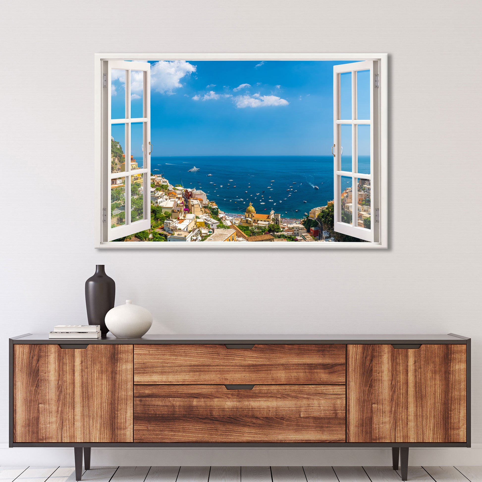 Ein realistisches Wandtattoo mit einem offenen Fensterblick auf eine malerische italienische Küstenstadt. Die Szene zeigt Positano an der Amalfiküste mit seinen bunten Häusern, einer kleinen Kirche und zahlreichen Booten, die auf dem tiefblauen Mittelmeer treiben. Der Himmel ist strahlend blau mit leichten Wolken. Das Wandbild verleiht dem Raum ein Gefühl von Weite und Urlaubsflair. Perfekt für eine entspannte und stilvolle Wohnatmosphäre.