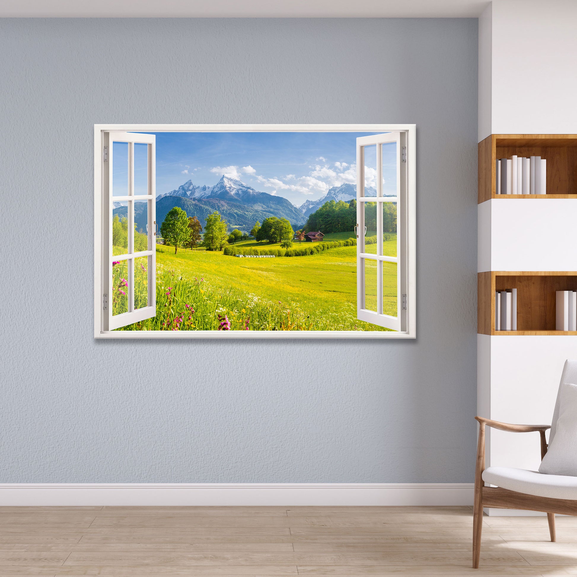 Leinwandbild mit offenem Fensterblick auf eine idyllische Berglandschaft mit grünen Wiesen, blühenden Blumen und schneebedeckten Gipfeln. Das Wandbild ist stilvoll in einem modernen Wohnzimmer mit blauen Wänden und Bücherregal integriert und sorgt für eine beruhigende und natürliche Atmosphäre.