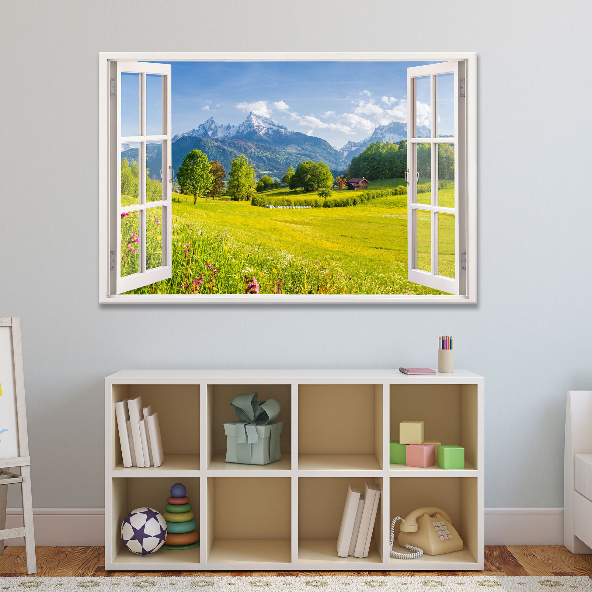 Leinwandbild mit offenem Fensterblick auf eine sonnige Berglandschaft mit grünen Wiesen und schneebedeckten Gipfeln, stilvoll integriert in ein gemütliches Kinderzimmer mit Regal und Spielzeug. Perfekte Wanddekoration für ein harmonisches Wohnambiente.
