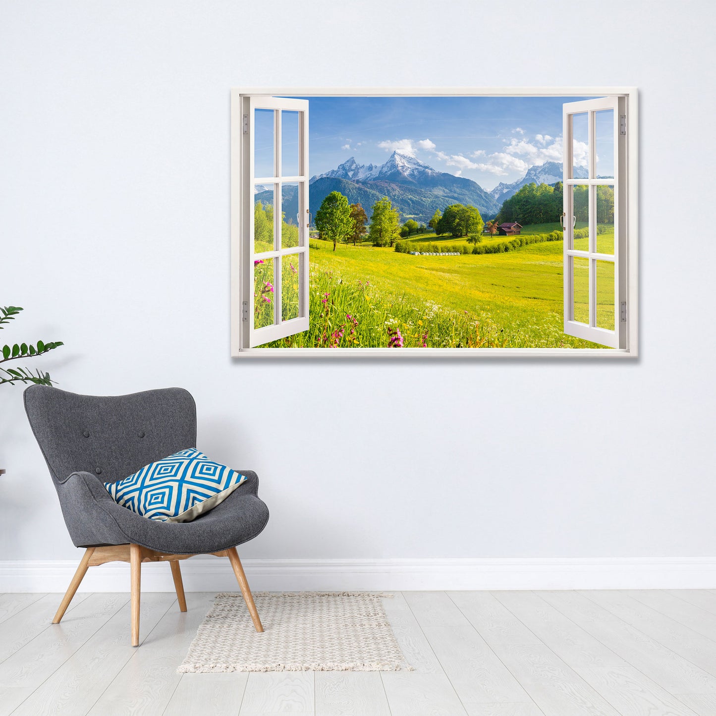 Moderne Wanddekoration mit offenem Fensterblick auf eine malerische Berglandschaft mit saftig grünen Wiesen und blühenden Blumen. Das Leinwandbild verleiht dem Wohnraum eine natürliche und entspannte Atmosphäre. Daneben steht ein stilvoller grauer Sessel mit blau gemustertem Kissen auf einem hellen Holzboden.