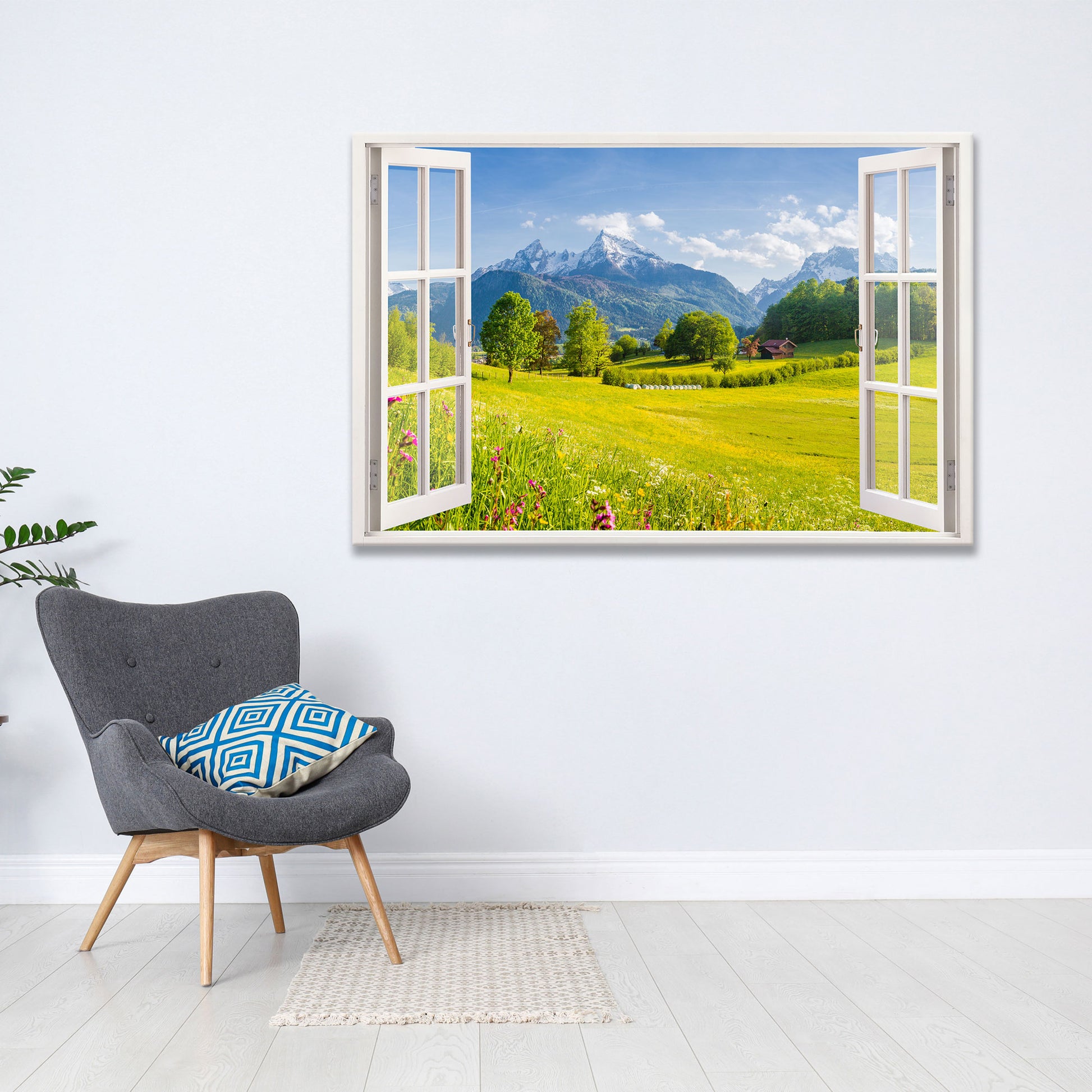 Moderne Wanddekoration mit offenem Fensterblick auf eine malerische Berglandschaft mit saftig grünen Wiesen und blühenden Blumen. Das Leinwandbild verleiht dem Wohnraum eine natürliche und entspannte Atmosphäre. Daneben steht ein stilvoller grauer Sessel mit blau gemustertem Kissen auf einem hellen Holzboden.