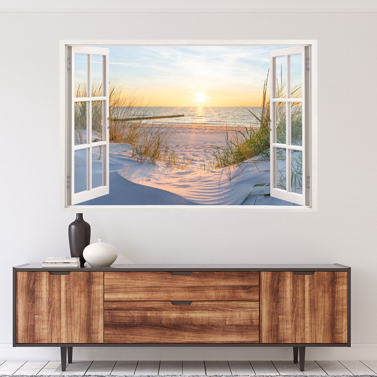 Wandtattoo mit offenem Fensterblick auf einen Sandstrand bei Sonnenuntergang. Die goldene Sonne spiegelt sich im ruhigen Meer, während sanfte Dünen mit Gräsern die Szene umrahmen. Perfekte Wanddekoration für eine entspannte, maritime Atmosphäre.