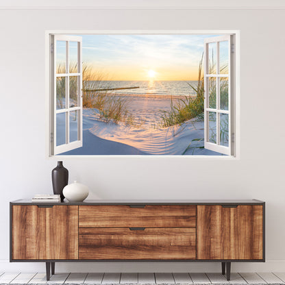 Wandtattoo mit offenem Fensterblick auf einen Sandstrand bei Sonnenuntergang. Die goldene Sonne spiegelt sich im ruhigen Meer, während sanfte Dünen mit Gräsern die Szene umrahmen. Perfekte Wanddekoration für eine entspannte, maritime Atmosphäre.